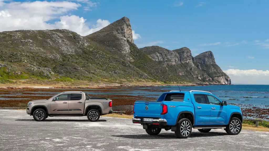 Two Volkswagen Amarok in PanAmericana and Aventura trims on a beach with a jagged mountain scene behind