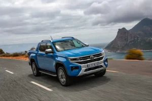 Volkswagen Amarok on a coastal road with a blue sea bay behind it and mountains