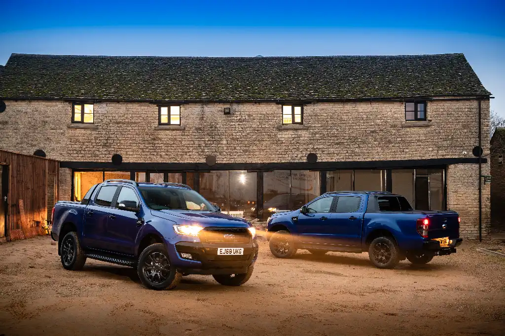 Two Ford Ranger Wildtrak X piack-ups with headlights on at dusk in front of a converted farmyard buliding 