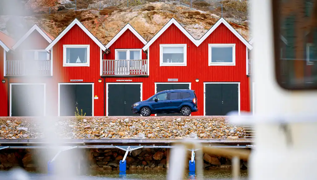 electric car parked next to a line of red fisherman's huts with a view through the rigging of a boat