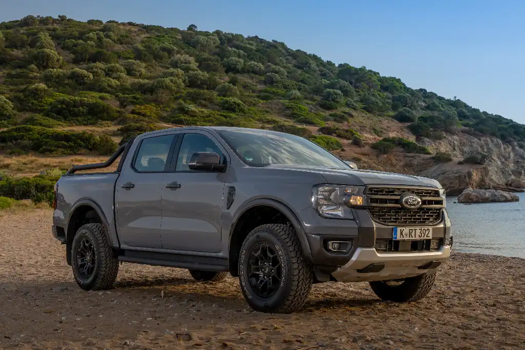 Ford Ranger Tremor in conquer grey on a stoney beach with the sea and a tree covered hill behind