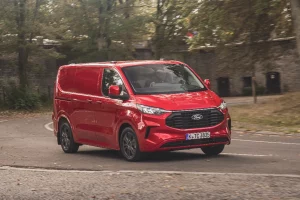 Ford Transit Custom in red cornering on a bend with a medieval stone wall behind