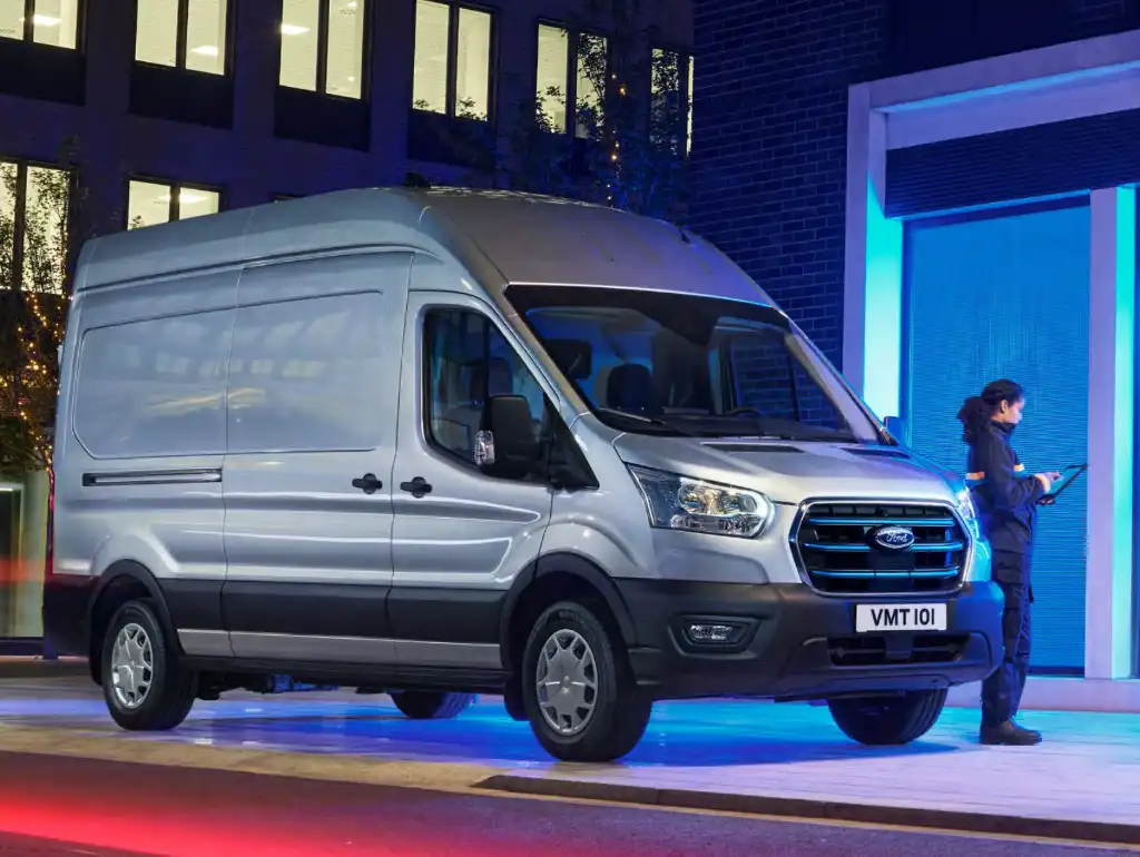 Ford E-Transit payload guide with a silver van on a blue street scene at night with a woman leaning agains the bonnet.